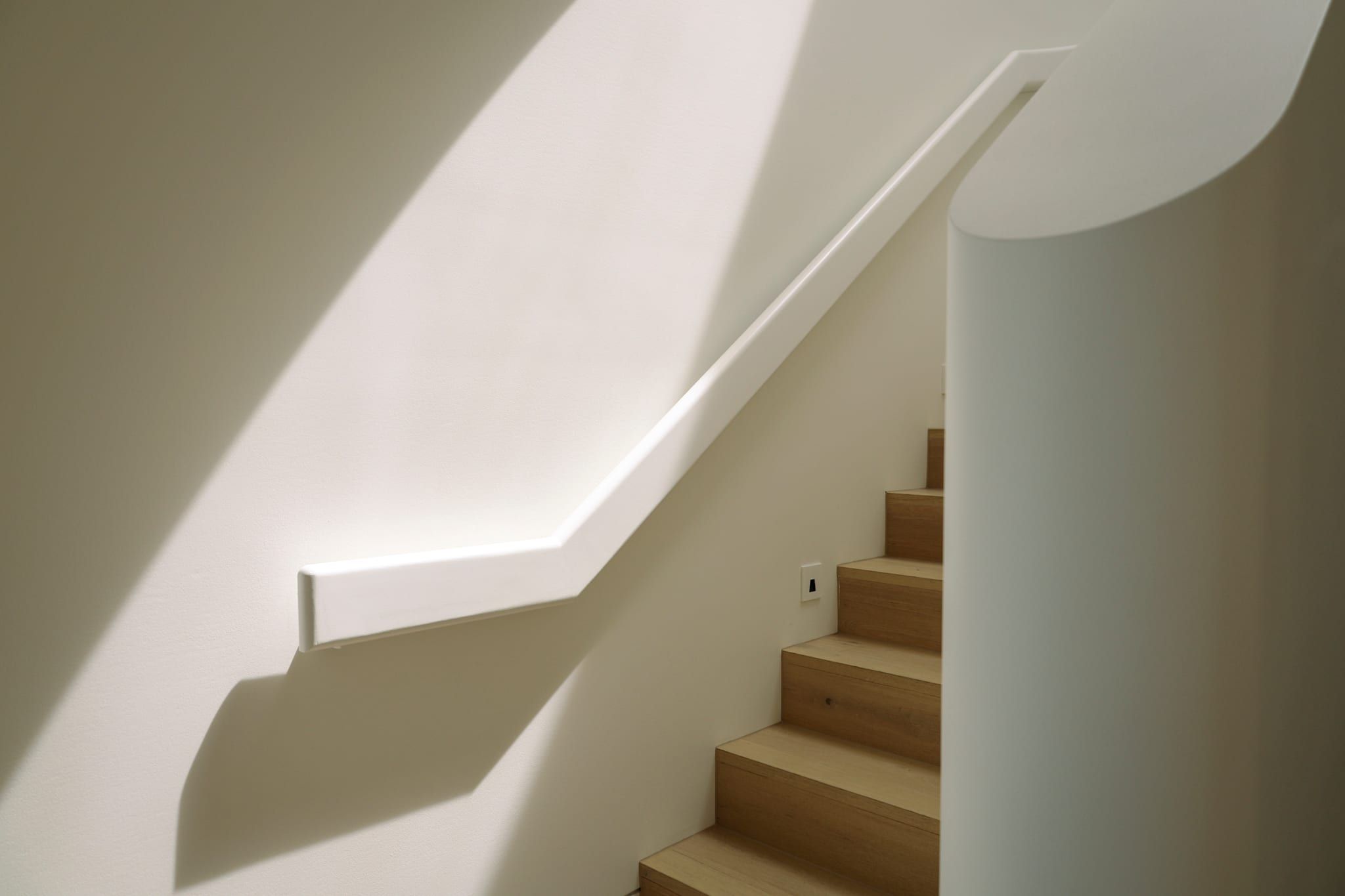 Sunlight across the curved plaster stair and handrail