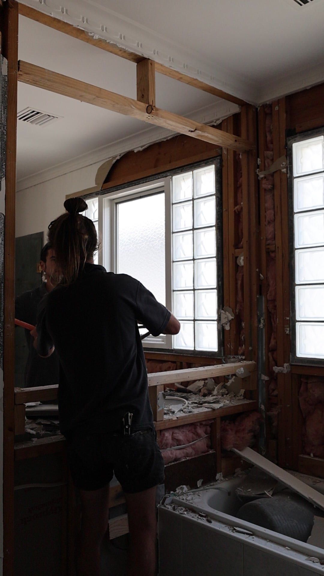 A period bathroom stripped back to its framing, with a glass-block window and original cornice above