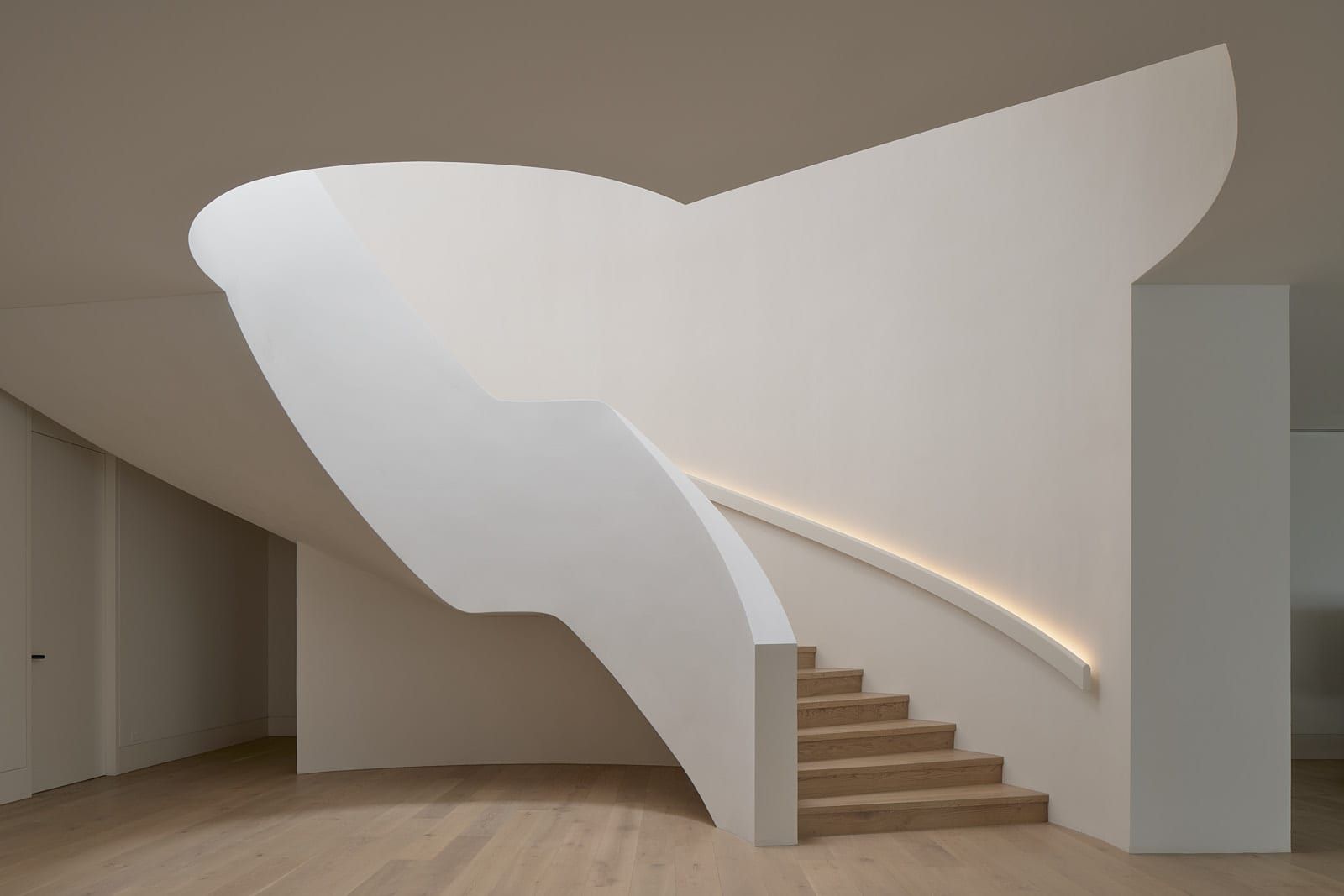 A sculpted curved plaster staircase rising through a calm, light-filled interior