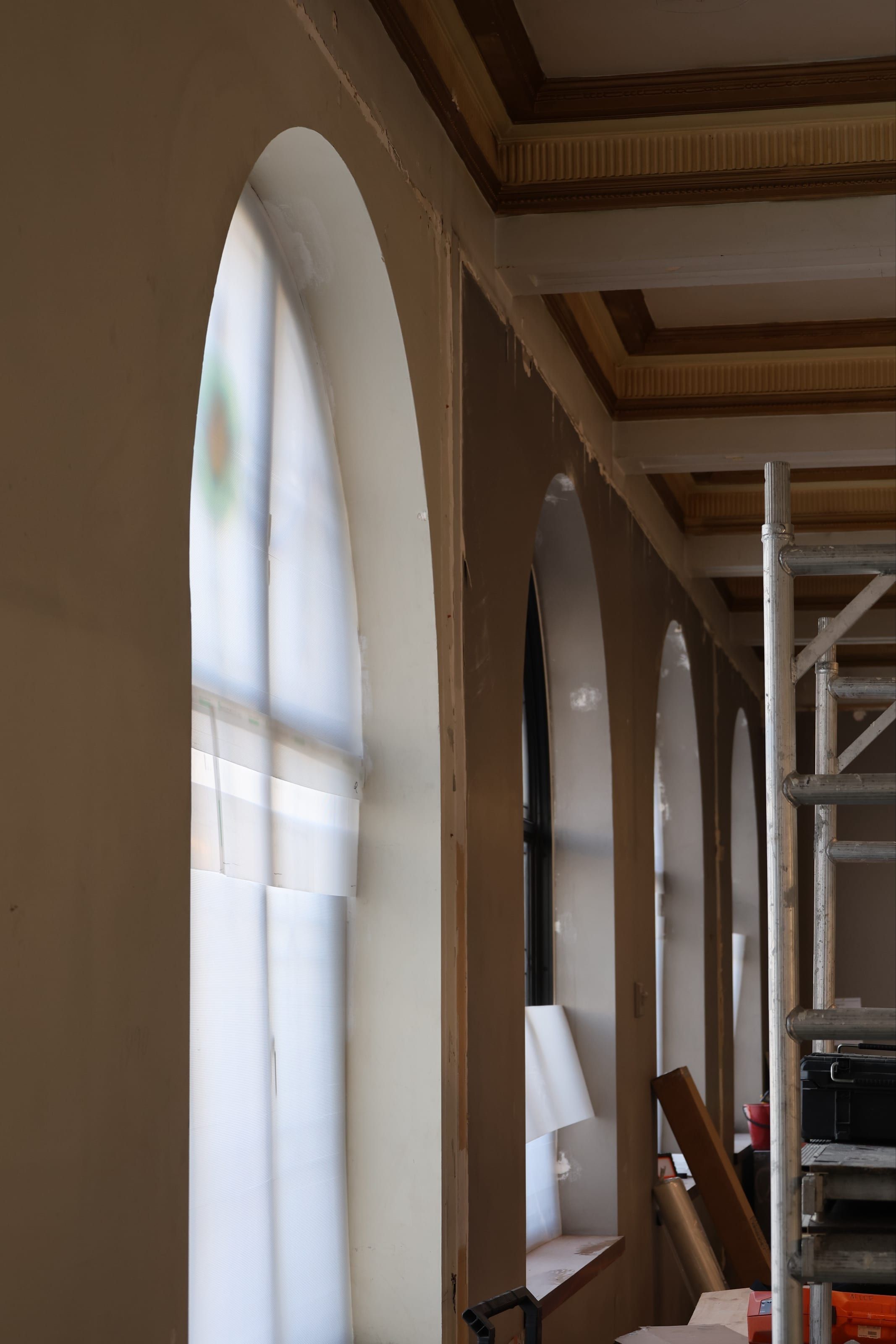 A row of arched openings beneath a gilded coffered ceiling, with scaffold in place
