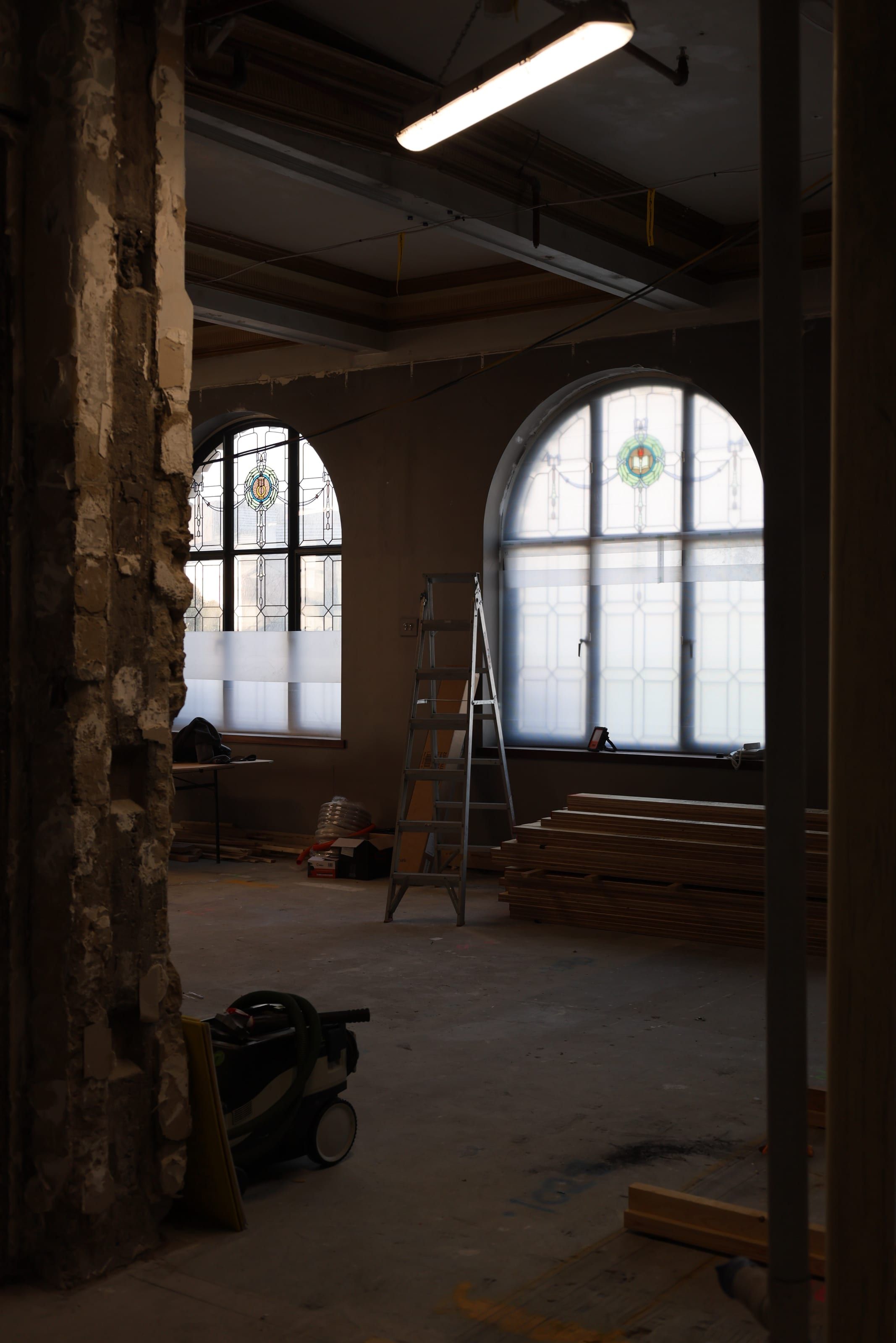 Arched leadlight windows and a gilded coffered ceiling beside a stripped-back masonry column, mid-restoration