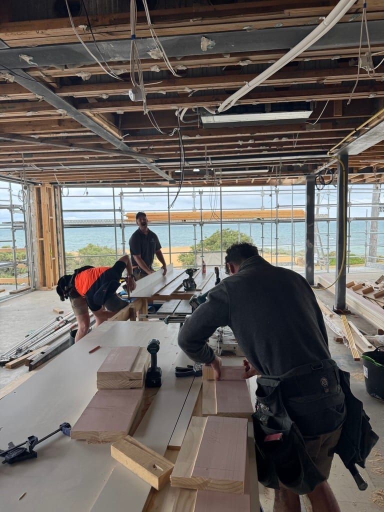 Two of the Siji crew setting out timber on the bench, the bay through the opening behind them